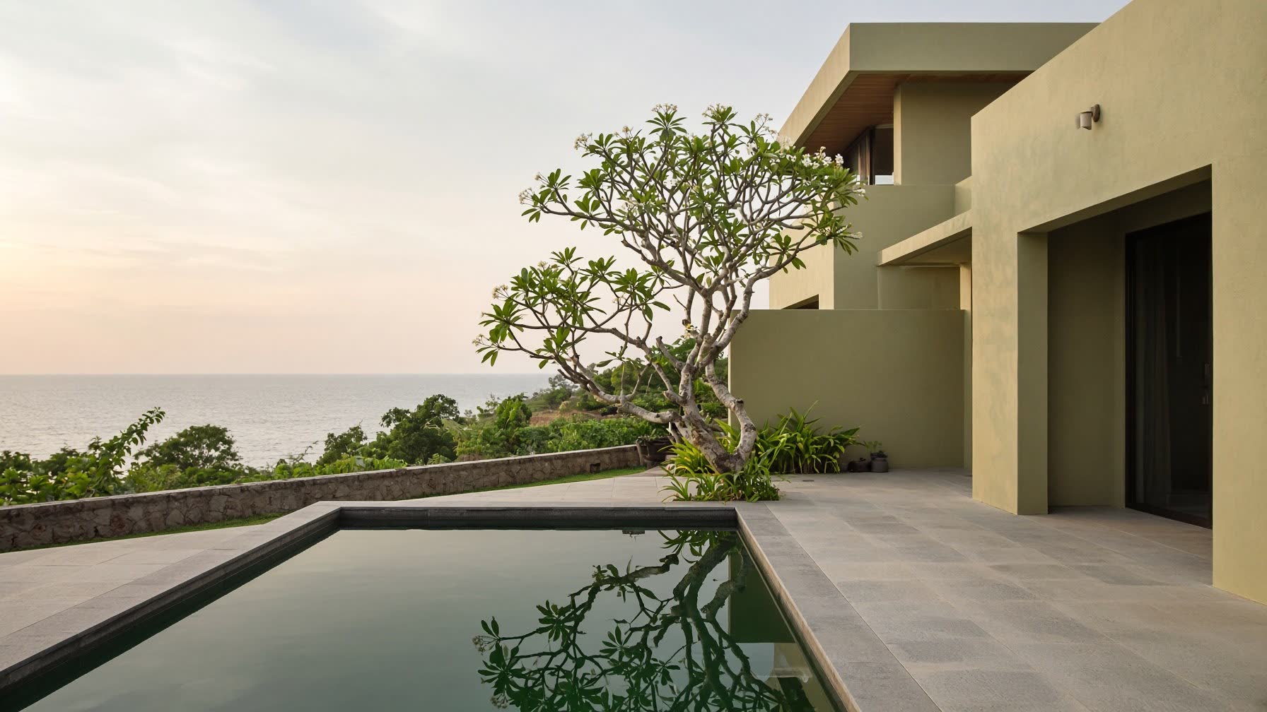 A contemporary Alibaug villa at late afternoon: still pool, lime-plaster walls, the sea beyond.